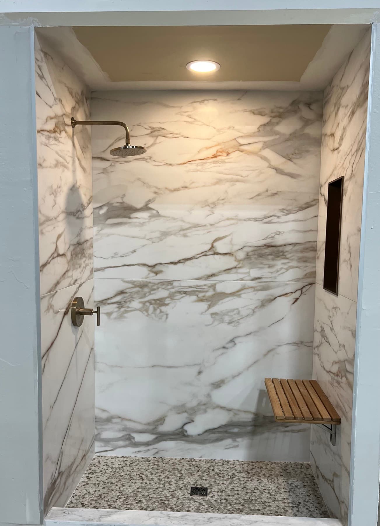 A folding bench and a dark-finish niche installed on porcelain shower walls
